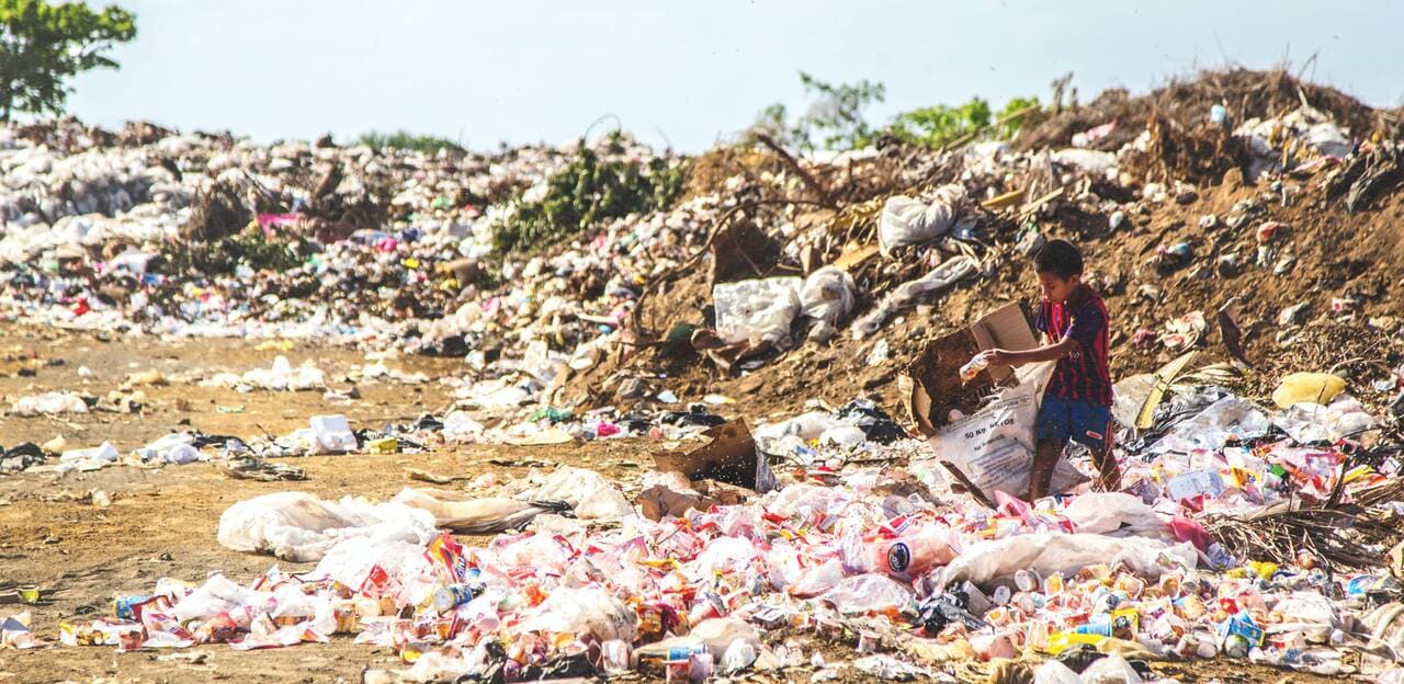 a boy in the middle of a lot of plastic waste collecting plastic bottles for recovery