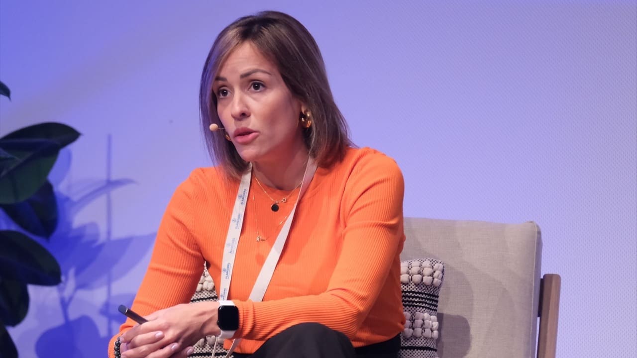 Ana Aguilar, COO of Plastiks, participates in a sustainability panel discussion. She wears an orange sweater and a headset microphone while addressing an audience about corporate transparency and blockchain-powered impact verification.